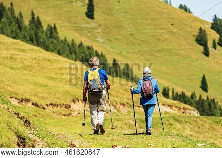 Feistritz An Der Gail, Austria - Aug 10, 2022: Two Hikers With Trekking Poles Walk On A Grassy Path 