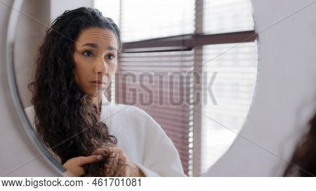 Worried Upset Young Woman Standing In Bathroom In Bathrobe Reflected In Mirror Looking At Split Ends