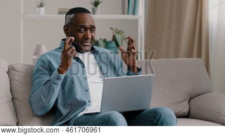 Mature African American Man Sitting At Home Looking At Laptop Screen With Hope Crossed Fingers Prayi
