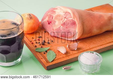 Close-up Of Raw Pork Knuckle, Dark Beer And Other Ingredients For Cooking Baked Pork Knuckle In Beer