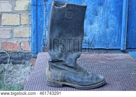 One Old Black Tarpaulin Boot Stands On A Brown Threshold Near A Blue Door In The Street