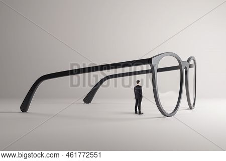 Thoughtful Young Guy Looking Through Abstract Huge Glasses On Gray Background. Clear Business Vision