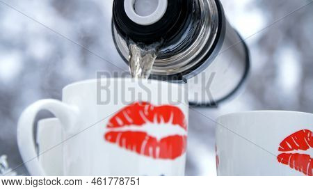 On A Background Of A Winter Forest, Close-up, From A Thermos Poured Tea Into Cups. On The Cups, Spon