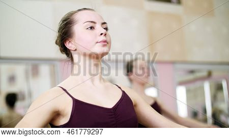 In Dancing Hall, Young Ballerina In Purple Leotard Performs A Certain Ballet Exercise, First Positio