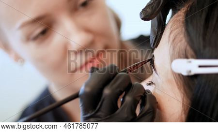 Close Up. Young Woman Gets Eyebrow Correction Procedure. Kosmetolog- Makeup Artist In Black Rubber G