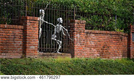 Two Skeletons Reach Through Iron Bars In Their Attempt To Escape.  Brick Wall Holds Iron Fencing.