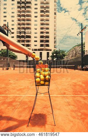 A Vertical Wide-angle View Of A Basket With Yellow Tennis Balls On An Orange Clay Court Surface And 