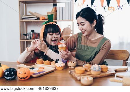 Young Girl And Mother At Halloween Making Treats And Cupcake On Table. Happy Halloween Day
