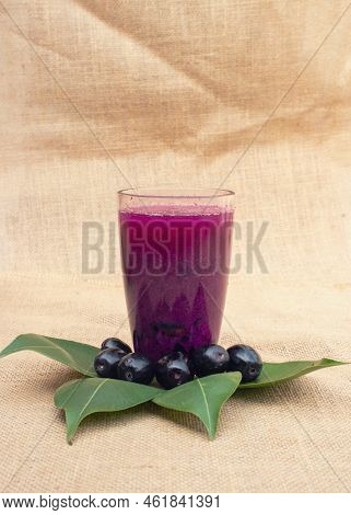 Closeup Of Jamun Or Syzygium Cumini Juice In A Glass With Fruit And Leaves Isolated On Burlap Fabric