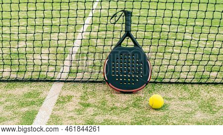 Yellow Ball On Grass Turf Near Padel Tennis Racket Behind Net In Green Court