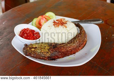Close Up Pecel Catfish Served On A White Plate Placed On A Wooden Table. Traditional Food From Indon