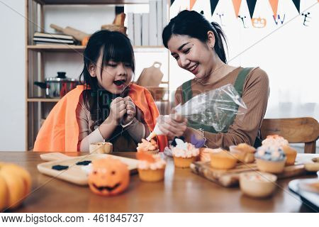 Young Girl And Mother At Halloween Making Treats And Cupcake On Table. Happy Halloween Day