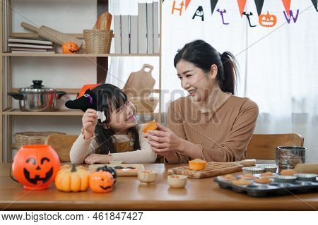 Young Girl And Mother At Halloween Making Treats And Cupcake On Table. Happy Halloween Day