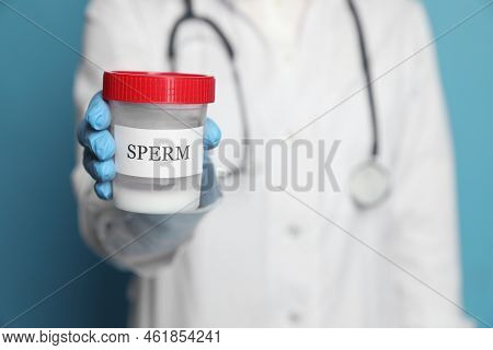 Doctor Holding Container With Sperm On Turquoise Background, Closeup. Space For Text