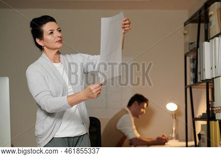 Portrait Of Pensive Serious Engineer Looking At Apartment Florr Plan In Hands