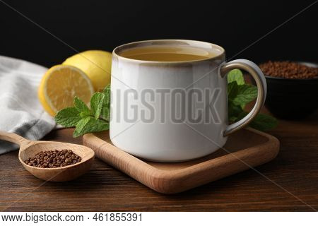 Cup Of Aromatic Buckwheat Tea, Spoon With Granules, Lemon And Mint On Wooden Table, Closeup