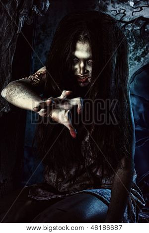Bloodthirsty zombi standing at the night cemetery in the mist and moonlight.