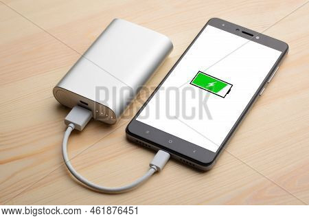 Modern Smartphone Lays On Light Wooden Table While Charging With Power Bank With Quick Charge. Illus
