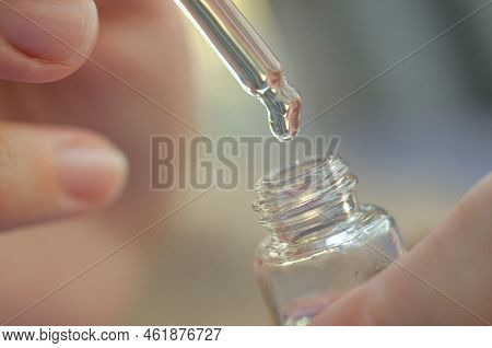 Serum Dripping From A Pipette Into A Bottle Close-up In Female Hands. A Drop Of Care Product Drippin