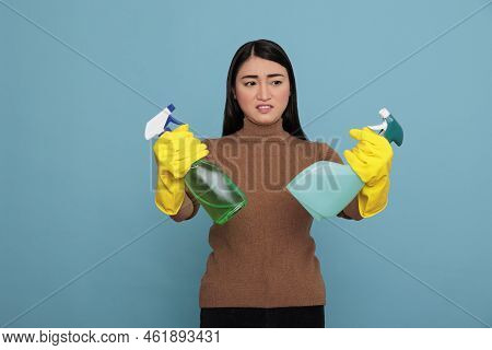 Asian Young Inactive Dull Housekeeper From Chores Holding Two Detergent Spray In Yellow Gloves Again
