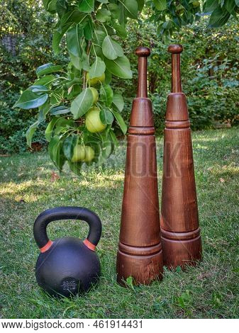 iron kettlebell and wooden Persian meels in a backyard with Asian pear tree, fitness concept