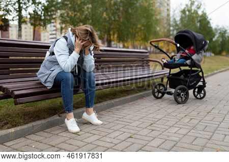 A Young Mother Sits On A Bench Upset Next To A Baby Stroller, Concept Of Postpartum Depression
