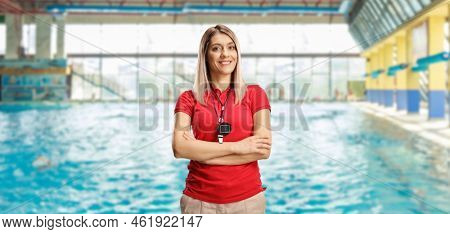 Female swimming coach with a wistle and stopwatch around her neck posing on an indoors swimming pool