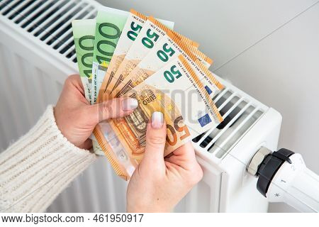Radiator And Euro Money Banknotes In Woman Hands. Expensive Gas Heating Cost. High Home Heating Bill