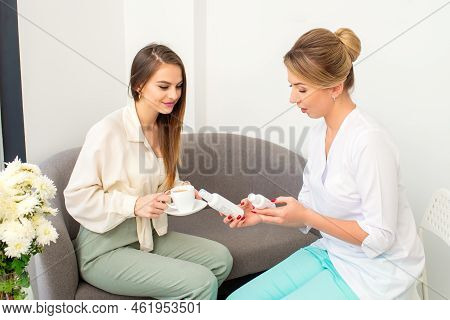 Beautician Offering Product For The Young Woman Holding White Plastic Bottles With A Cream Sitting O
