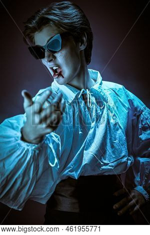 Halloween vampire party. Cool teenage vampire in elegant white shirt and party sunglasses sings and dances with verve. Studio portrait. 
