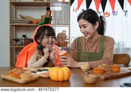 Young Girl And Mother At Halloween Making Treats And Cupcake On Table. Happy Halloween Day