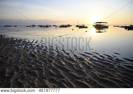 Golden Glow Of The Sun Rising At Dawn  Silhouettes Fishing Boats At Sanur Beach, Bali Indonesia.
