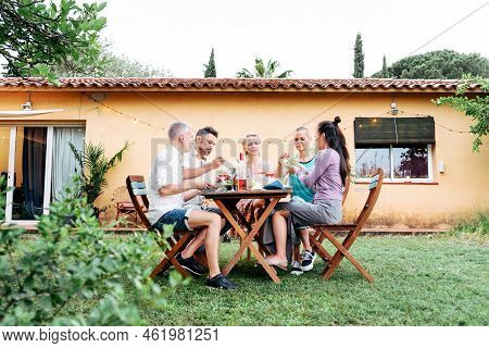 Longview Of A Group Of A Adult Friends Having A Dinner Party In The House Backyard With Beer And Win