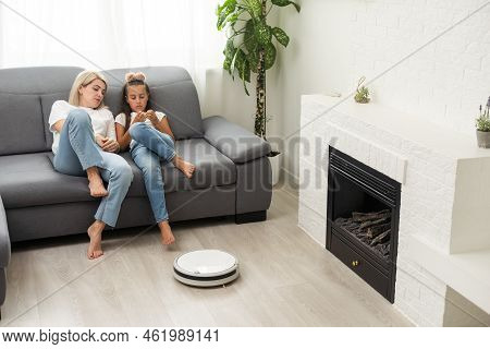 Cute Child Near Mother Looking At Robotic Vacuum Cleaner In Living Room