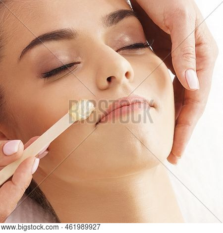 Hair removal, beauty and health concept. A young girl is getting an epilation procedure. A processional beauty worker is making depilation with hot wax.