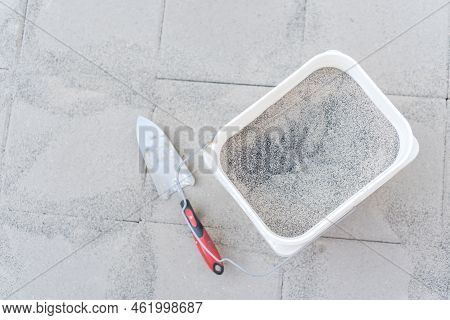 Full Bucket Of Polymeric Paver Sand With Trowel On Top Of Gray Concrete Patio Stone Paver Walkway