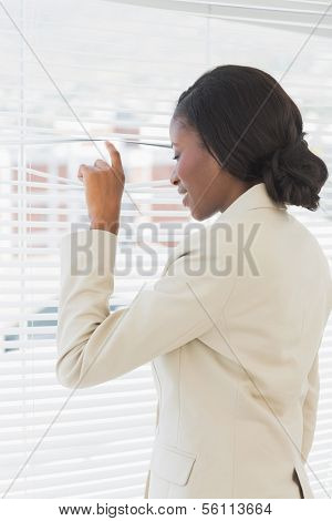 Rear view of a young businesswoman peeking through blinds in office