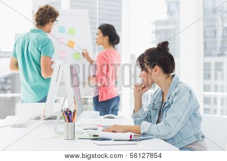 Side view of a casual woman using computer with group of colleagues behind in a bright office