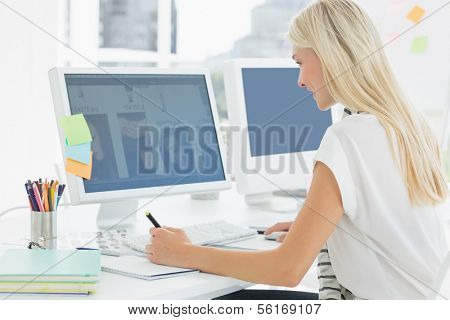 Side view of a casual young woman using computer in a bright office