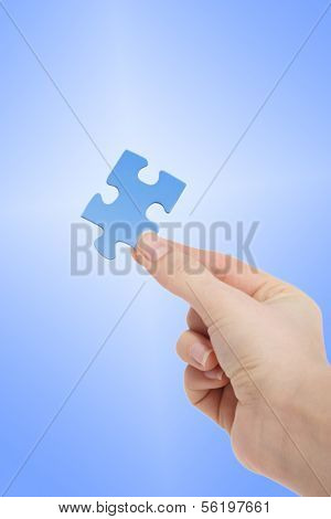 A person holding a blue piece of a puzzle in his hand in front of a white to blue gradient