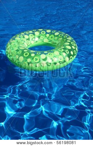 An inflatable green plastic ring swimming in a shiny blue swimming pool.