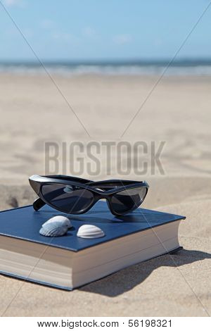 A book and sunglasses lying in the sand, symbolizing recreation