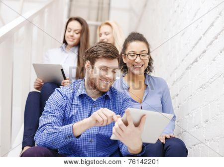 business, technology and startup concept - smiling creative team with tablet pc computer sitting on staircase