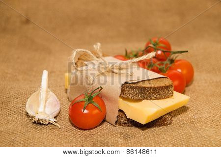 Sandwich With Cheese Wrapped In Paper, Cherry Tomatoes And Garlic On Old Cloth