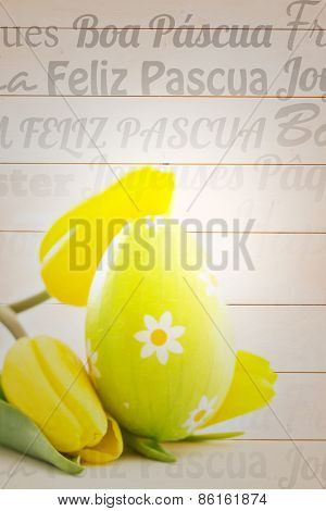 Happy easter in different languages against green easter egg with yellow tulips