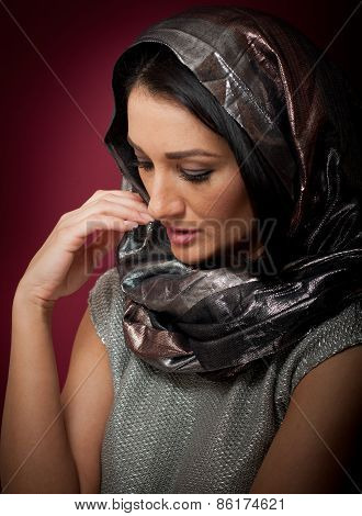 Attractive brunette woman in gray blouse and headscarf posing dramatic on purple background