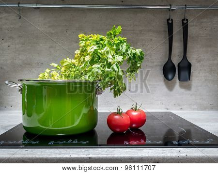 Green enamel stewpot with parsley and two tomatoes on black induction cooker
