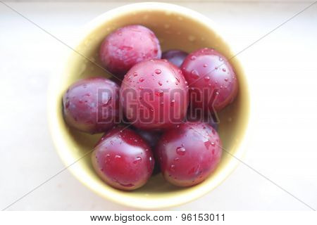 plums in a yellow bowl on a white background