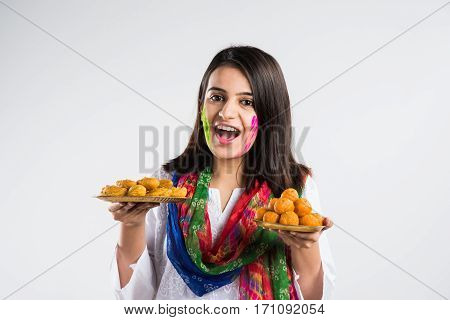 indian pretty young girl holding a plate full of sweet bundi laddu or gujiya and powder colour called gulal or gulaal on indian festival called Holi, isolated over white background, selective focus