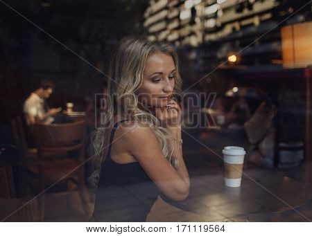 Beautiful blonde girl sitting at the cafe with a cup of coffee and a figure of man behind her on the background. Romantic concept. Blind date. Lonely in Saint Valentine. Relationship concept.